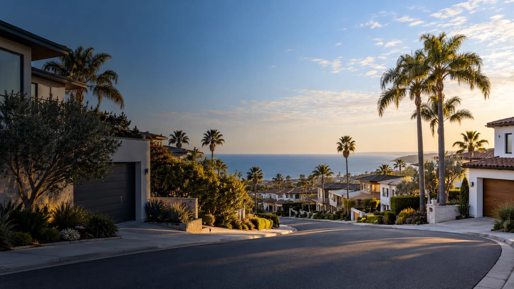 A quiet residential street lined with palm trees, with the ocean in the distance